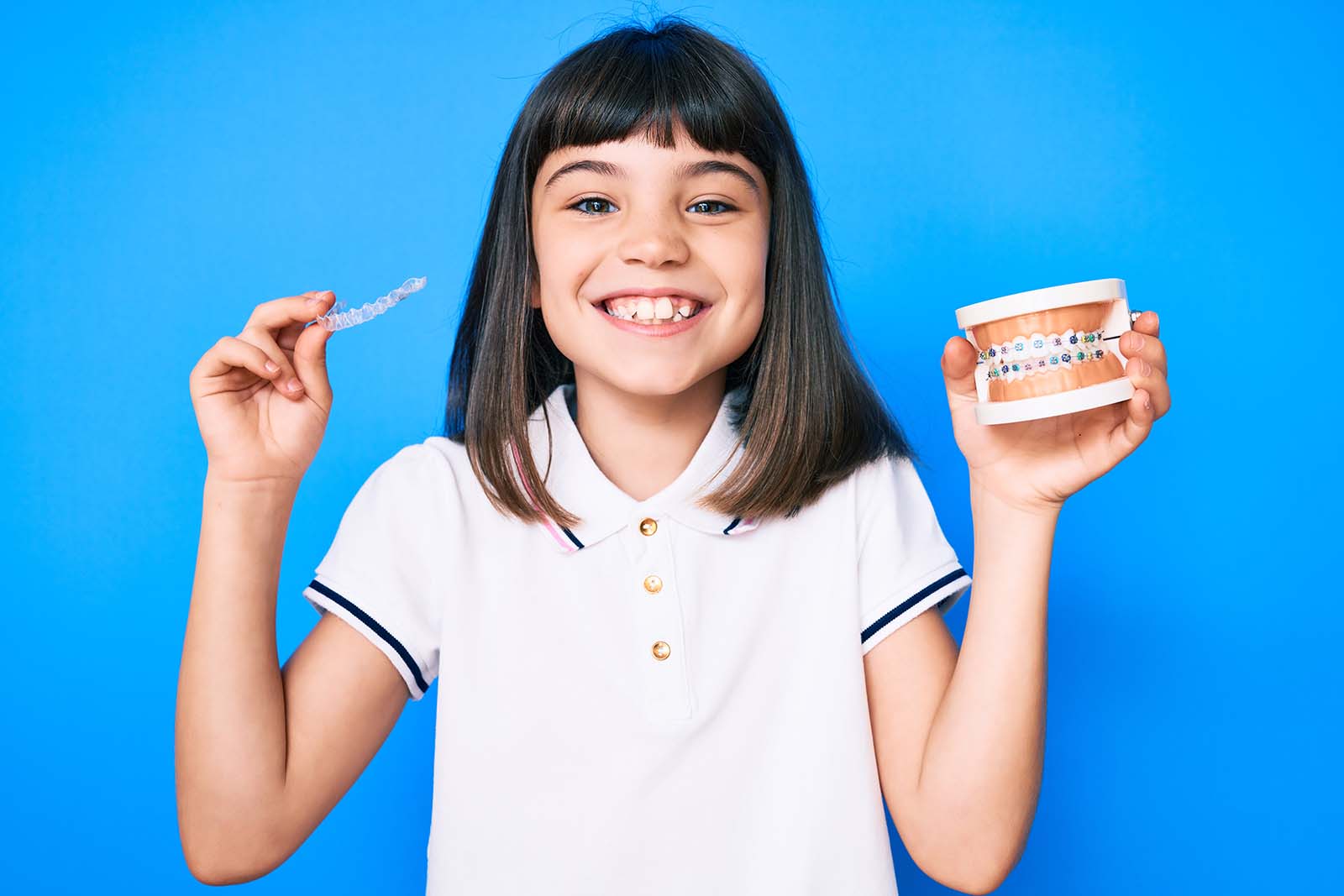 Happy little girl holding invisalign aligners and braces