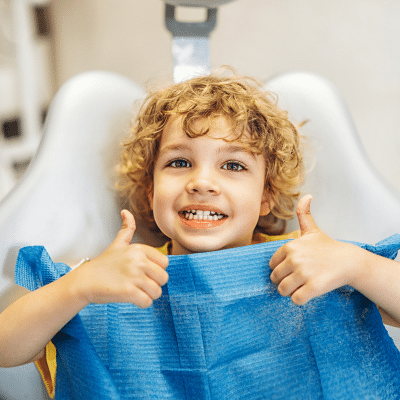 Young boy at dentist giving two thumbs up after emergency dental care