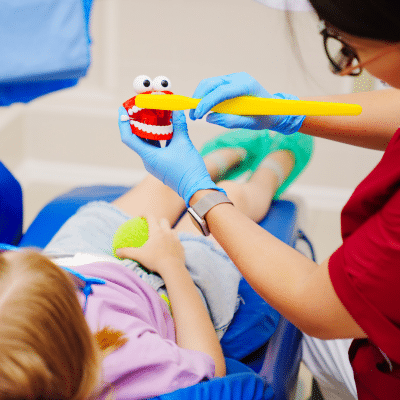 Dentist illustrating to a kid how to brush teeth with toy teeth, representing pediatric dentistry