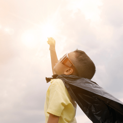 Little boy wearing a cape, holding his arm up like he's super man, representing oral hygiene dental apps