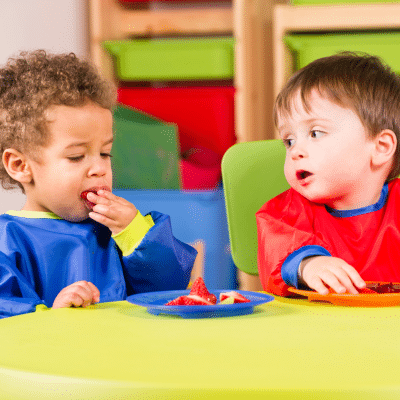Two little boys sitting at a yellow table with toys, representing tooth decay in toddlers
