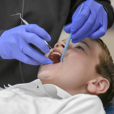 A dentist using dental tools to work on a little boy's mouth, representing what to do if your child has a toothache
